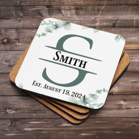 A product image of a rounded corner beverage coaster with a cork back, high gloss front, and printed with watercolor greenery and a monogram with your name and date family was established
