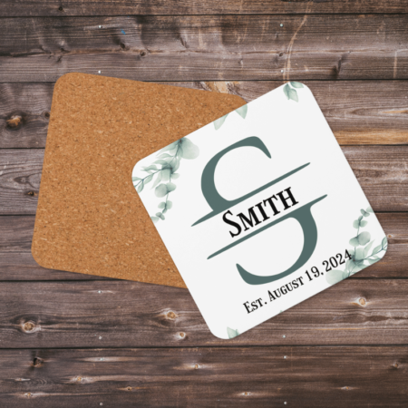 A product image of a rounded corner beverage coaster with a cork back, high gloss front, and printed with watercolor greenery and a monogram with your name and date family was established