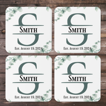 A product image of a rounded corner beverage coaster with a cork back, high gloss front, and printed with watercolor greenery and a monogram with your name and date family was established