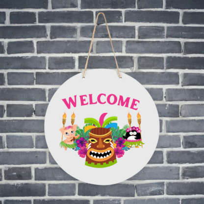 A product image of a hanging welcome sign with a luau theme, printed with a penguin and a pig in grass skirts, with tropical flowers, tiki torches, and a tribal mask